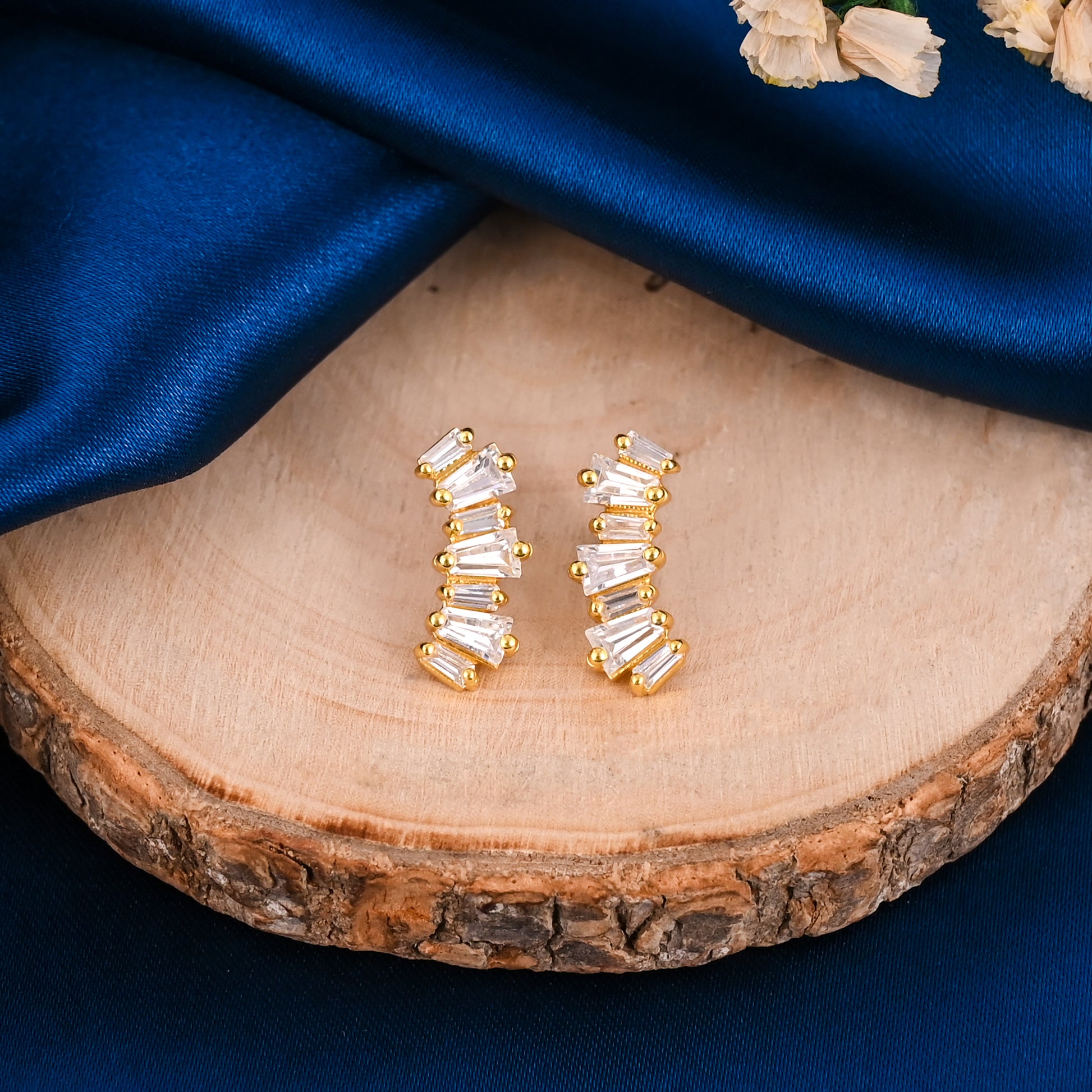 Gold earrings with clear stones on a wooden surface with blue fabric background