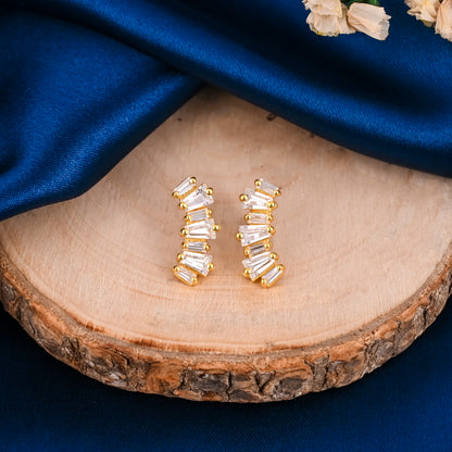 Gold earrings with clear stones on a wooden surface with blue fabric background