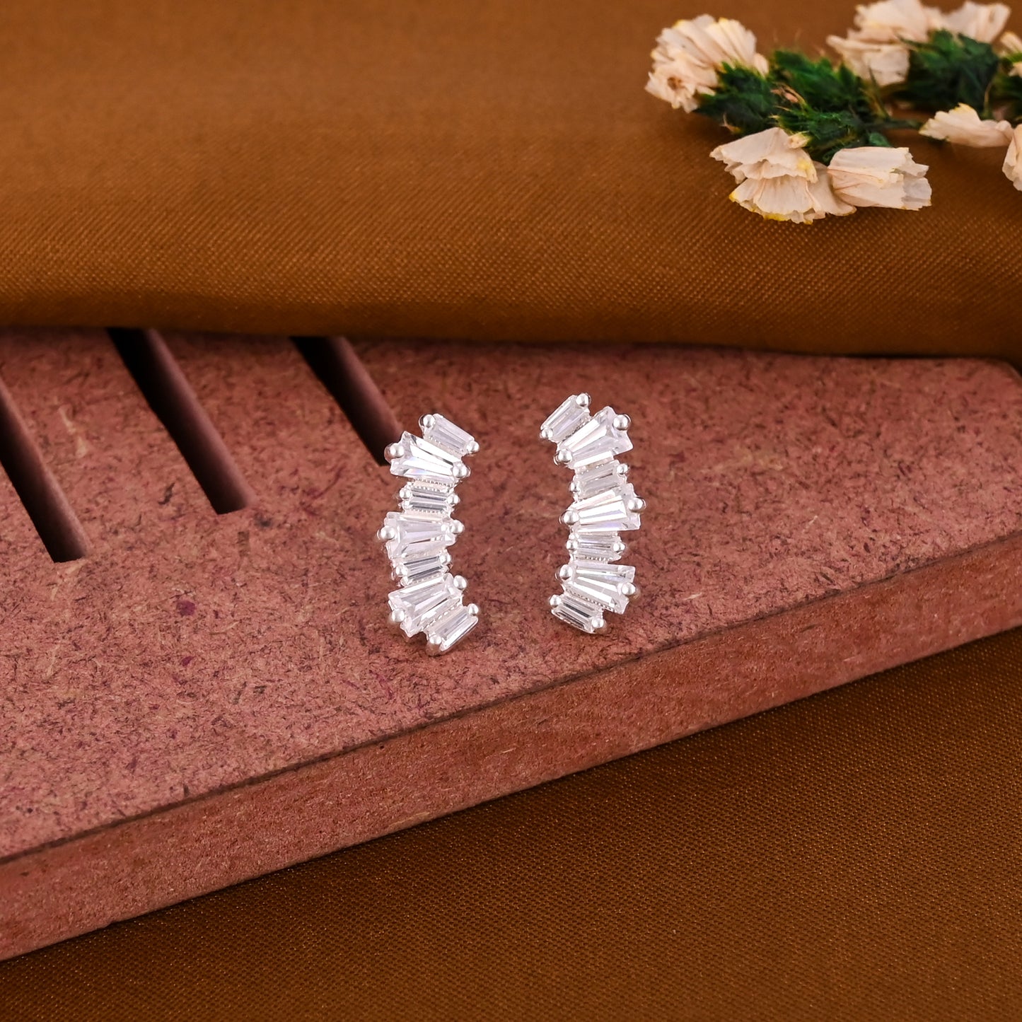 Pair of silver hoop earrings on a textured brown surface with decorative flowers.