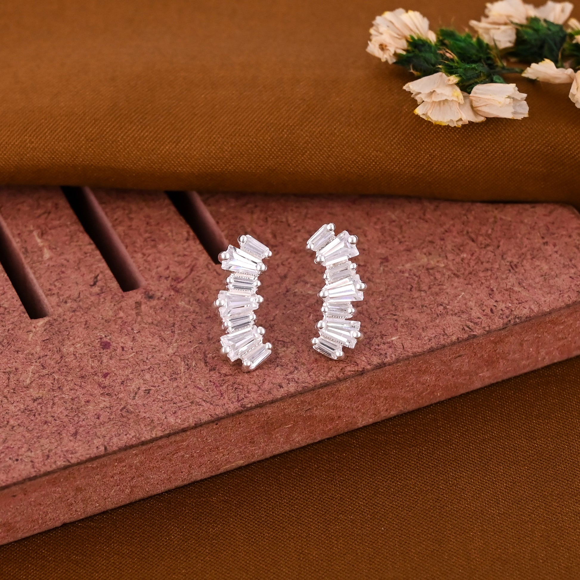 Pair of silver hoop earrings on a textured brown surface with decorative flowers.