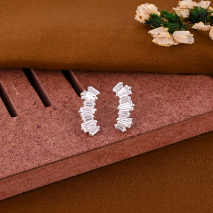 Pair of silver hoop earrings on a textured brown surface with decorative flowers.