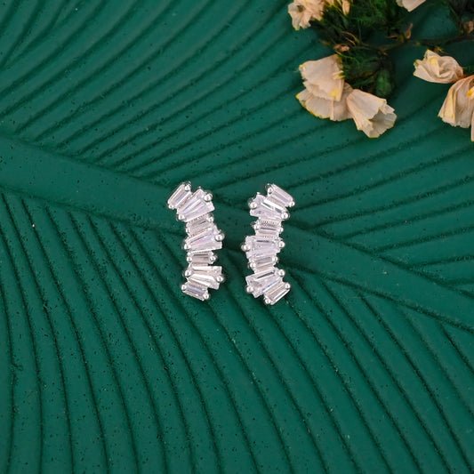 Silver earrings on a textured green surface with flowers in the background